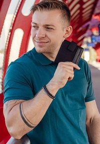 Black leather wallet with a clasp, held by a person wearing a teal polo shirt, on a red and metal-patterned background.