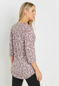 Maroon kukkatrikoo, jossa on kolmanneksen pituiset hihat, valkoiset kukkakuviot, pyöristetty helma ja rento mitoitus. Sileä kankaan tekstuuri.