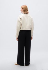 Κομμένο μπεζ σακάκι με κουμπιά στο μπροστινό μέρος, σε συνδυασμό με μαύρο παντελόνι φαρδύ και αθλητικά παπούτσια, από πίσω όψη.