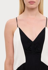 Czarna i biała sukienka z cienkimi ramiączkami, dekoltem w kształcie litery V, marszczeniem na środku oraz mieszanką fakturowanych tkanin.