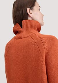 Orange gestrickter Pullover mit hohem, gefaltetem Kragen. Verfügt über eine gerippte Textur und diagonale Nahtdetails an den Schultern.