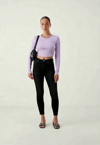 Lilak värviga lühikesed pikkade varrukatega topp, mustad kitsad teksad ja mustad sildiga sandaalid hõbedaste aktsentidega. Lihtne disain ja istuv siluett.