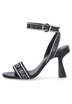 Sandale à talons hauts noire en matériau brillant, dotée d'une bride avant avec imprimé logo blanc et d'une sangle de cheville ajustable avec une boucle en argent.