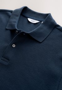 Polo blu navy scuro con trama, maniche corte, collo, pattina con due bottoni ed etichetta "NEXT Regular Fit" all'interno del collo.