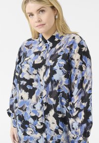 Langärmliges Hemd aus mehrfarbigem Stoff mit einem abstrakten Muster in Blau, Schwarz und Creme, mit Knopfleiste und Kragen.