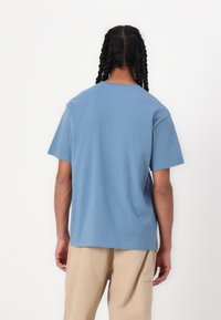 T-shirt en coton bleu clair à manches courtes, avec un col rond et une coupe droite. Le dos présente une finition lisse sans motifs ni accents.