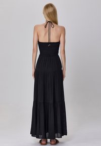 Robe maxi noire avec un corsage froncé et une jupe à volants, dotée d'un col halter avec des liens ajustables et une texture fluide.