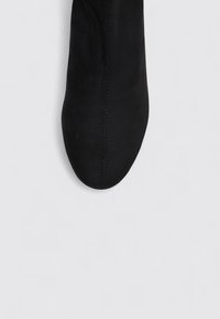 Black suede ankle boot with a smooth texture, rounded toe, and side seam stitching. Minimalist design, no visible hardware or accents.