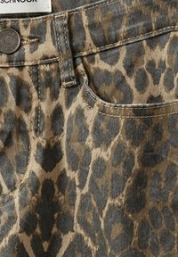 Leopardmönstrad denimtyg med en blandning av tan- och bruna nyanser, med en texturerad yta, metallknapp och kontrasterande sömnadsdetaljer.