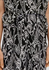 Schwarz-weißer Stoff mit einem gerippten Muster, das ein florales Design zeigt; geraffte Taillenpartie; kurze Ärmel.
