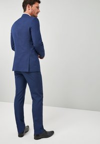 Marineblauer Anzug mit taillierter Passform, ausgestattet mit einem einzelnen Schlitz im Sakko und schmal geschnittenen Hosen. Glänzende schwarze Dressschuhe runden den Look ab.