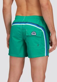 Pantaloni da bagno verdi con tasca posteriore, caratterizzati da strisce blu e bianche lungo i lati. Realizzati in materiale leggero e morbido.