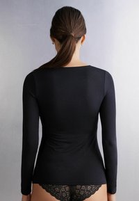 Zwarte langemouwen top met een ronde halslijn, aansluitend ontwerp en een gladde textuur, gecombineerd met zwart ondergoed met kant dat zichtbaar is bij de taille.