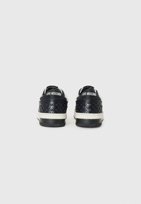 Zwarte sneakers met een gestructureerd hartpatroon, witte logo op de hiel en contrasterende witte zool. Gladde materialen en laag gesneden ontwerp.