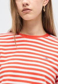 Young woman wearing a red and white striped shirt with gold hoop earrings, close-up on neck and upper chest.