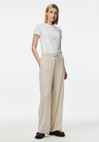 T-shirt blanc à manches courtes associé à un pantalon en lin beige, ample, avec taille élastique et cordon de serrage, porté avec des chaussures noires.
