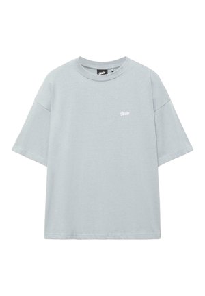 Lichtgrijs oversized T-shirt met korte mouwen, ronde hals en klein wit logo op de linkerborst, tegen een witte achtergrond.