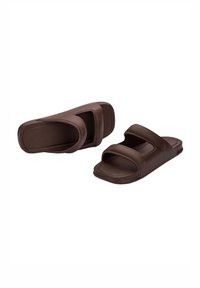 Bruna slip-on sandaler med två breda remmar, platta sulor och en glIDande yta, tillverkade av ett hållbart material som är lämpligt för avslappnad användning.