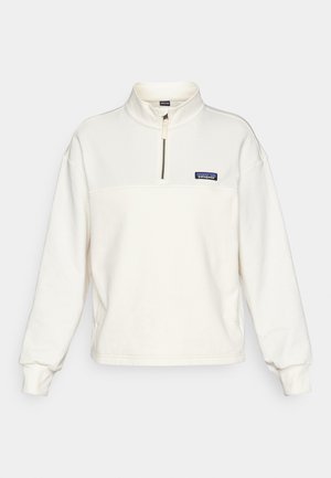 Pulover iz kremaste flisaste tkanine s polovičnim zadrgo, dolgimi rokavi in majhnim modrim logotipom Patagonia na prsih. Gladka tekstura.