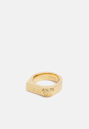 Bague carrée en or avec un emblème tête de Méduse et "Versace" gravé sur le côté, présentée sur fond blanc.