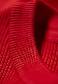 Primo piano di tessuto a maglia red ribbed con texture e pieghe visibili, che mette in risalto il motivo e la morbidezza del materiale.