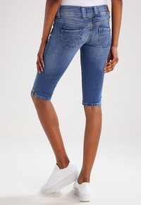 Siniset farkkukaprihousut, joissa on istuva malli, takataskut ja hieman rispaantunut helma. Yhdistetty valkoisiin lenkkareihin.