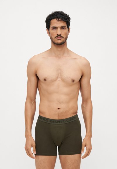 Olíva zöld boxer alsónemű, puha, rugalmas anyagból, fekete "POLO RALPH LAUREN" felirattal ellátott derékrésszel. A modell a karjait az oldalán tartja.