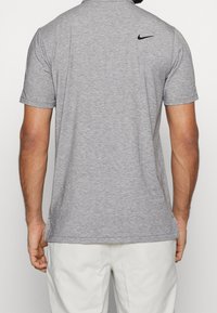 Graues Poloshirt mit kurzen Ärmeln und feiner Struktur, präsentiert mit einem schwarzen Nike-Logo am hinteren Kragen und einem geraden Saum.