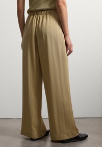Weite Hosen aus leichtem, cremefarbenem Stoff mit einer strukturierten Oberfläche und einem elastischen Bund.