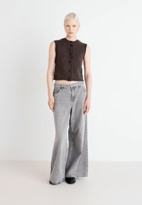 Hnědý pletený bezrukávový top s pěti knoflíky, doplněný o šedé vysoké široké džíny a černé boty. Jednoduchý, casual design.
