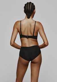 Conjunto de lencería negra que incluye un bralette ajustado con tirantes ajustables y una parte inferior de cintura alta, fabricado en un tejido suave, con un diseño minimalista.