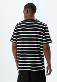 Sort og hvid stribet t-shirt med korte ærmer, rund hals og afslappet pasform. Materialet er bomuld med en glat tekstur og kontrasterende striber.