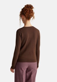 Brązowy sweter dzianinowy z okrągłym dekoltem i ściągaczami, w zestawie z kraciastymi spodniami. Miękka textura z dopasowaną sylwetką.