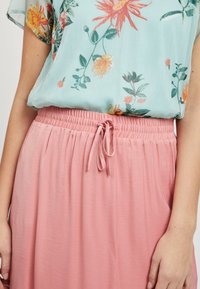 Blouse à fleurs bleu clair avec une jupe rose à taille élastique. La jupe possède un lien pour l'ajustement et une texture lisse avec une coupe ample.