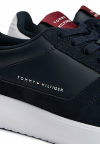 Sneaker navy blue di Tommy Hilfiger con suola bianca, lacci navy, pannelli in suede e pelle, e etichetta del marchio rossa sulla linguetta.