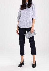 Koszula w paski z podwiniętymi rękawami, do której dobrano granatowe spodnie w delikatne paski. Trzyma teksturowaną szaro-skalną kopertówkę i ma na sobie czarne buty na obcasie.