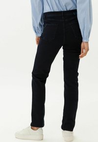 Úzké džíny v tmavě modrém denimu, s pěti kapsami a jemnými detaily šití. V kombinaci s bílými teniskami. Hladká textura, přiléhavý design.