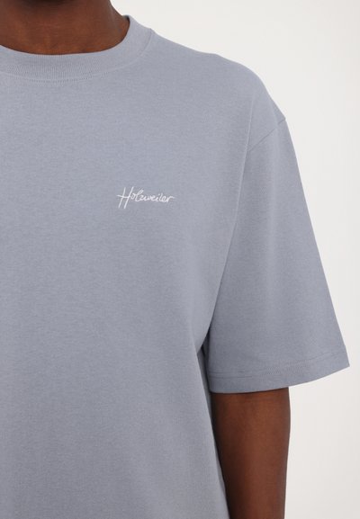 Light blue cotton t-shirt with short sleeves, featuring a small white embroidered logo on the left chest area and a crew neck design.