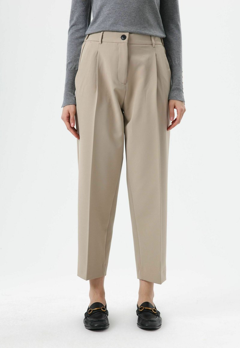 Beige tailored trousers with a high waist, pleats, and a straight leg design, paired with black loafers, featuring a silver accent.