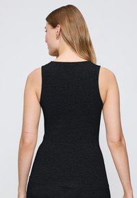 Czarny bezrękawnik o dopasowanym kroju, wykonany z teksturowanej tkaniny. Wyróżniające się detale to gładkie ramiona i zaokrąglony dół.