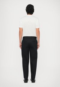 Biała bawełniana koszulka z krótkimi rękawami, zestawiona z czarnymi spodniami i czarnymi butami. Prosty fason, dopasowany krój i minimalistyczny styl.