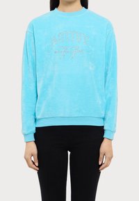 Sudadera azul cielo con una textura suave, que presenta un logo "ACTIVE 77" adornado con cristales. Mangas largas y puños acanalados.