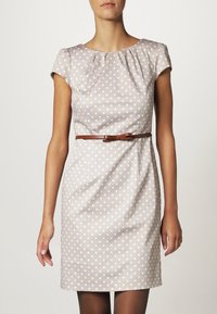 Abito beige con pois bianchi, maniche corte a campana, scollatura plissettata e una cintura marrone in vita. Tessuto liscio con vestibilità su misura.