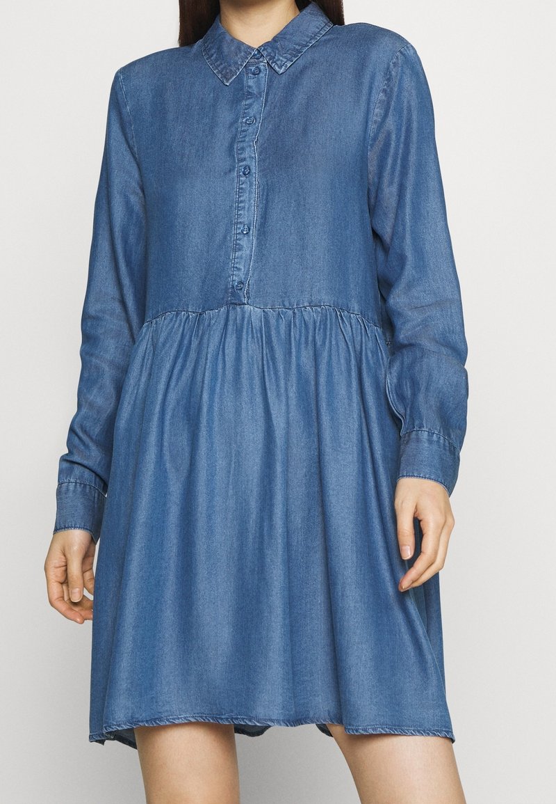 Robe en denim avec un col, une fermeture à boutons et des manches longues. La taille froncée crée une silhouette évasée. Couleur bleu clair.