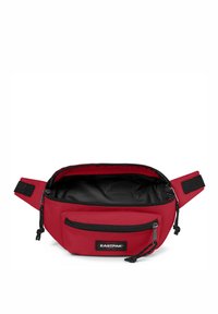 Červený bum bag Eastpak vyrobený z odolné tkaniny, s hlavní komorou s černým interiérem, nastavitelným popruhem a přední kapsou na zip.
