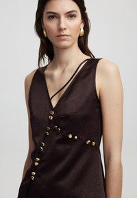 Dark brown sleeveless dress with a v-neck, featuring textured fabric and gold-tone buttons along the front and thin shoulder straps.