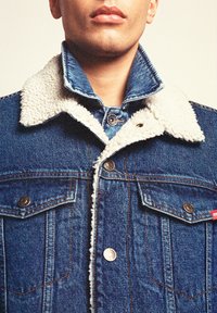 Denim jope, millel on sinine välimus, valge fliisikrae, metallnupud ja kaks rinna taskut klappidega.