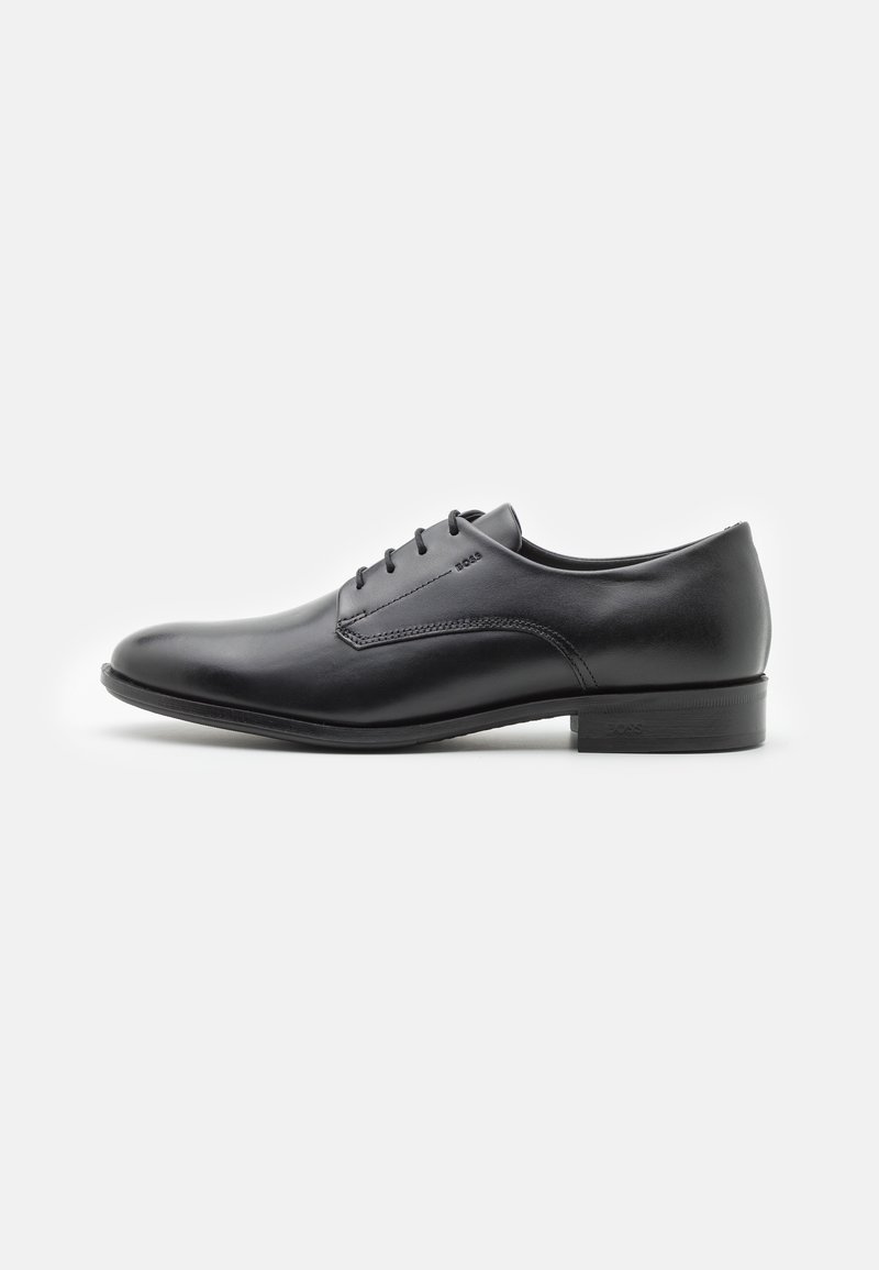Chaussure en cuir noir avec une finition lisse, bout arrondi, et cinq œillets pour les lacets. Présente un petit talon empilé et un logo minimal.