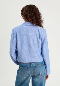 Veste en lin bleu cropped avec une finition texturée et un col cranté, associée à un jean en denim taille haute avec des poches arrière.