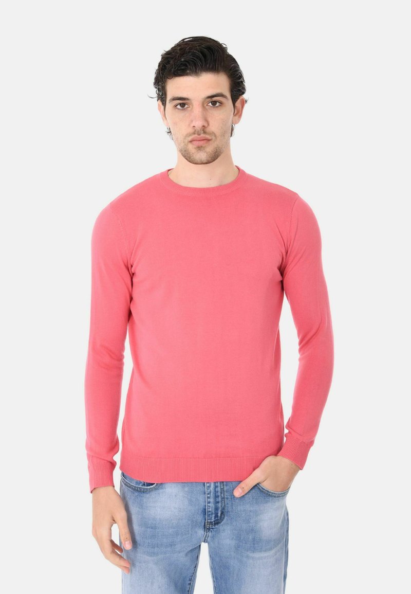 Maglione a maniche lunghe rosa chiaro con scollatura rotonda. Vestibilità slim e polsini a costine. Abbinato a jeans in denim azzurro.
